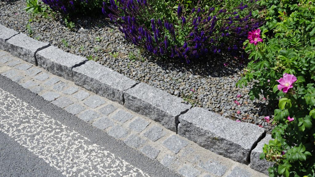 Žulové obrubníky podél silnice a záhonu – přírodní kámen jako trvanlivé a estetické řešení okraje cesty.