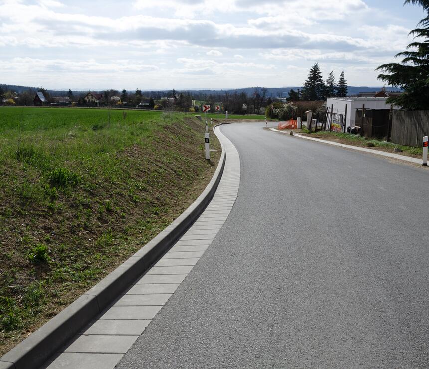 Betonová silniční přídlažba podél asfaltové cesty v otevřené krajině.