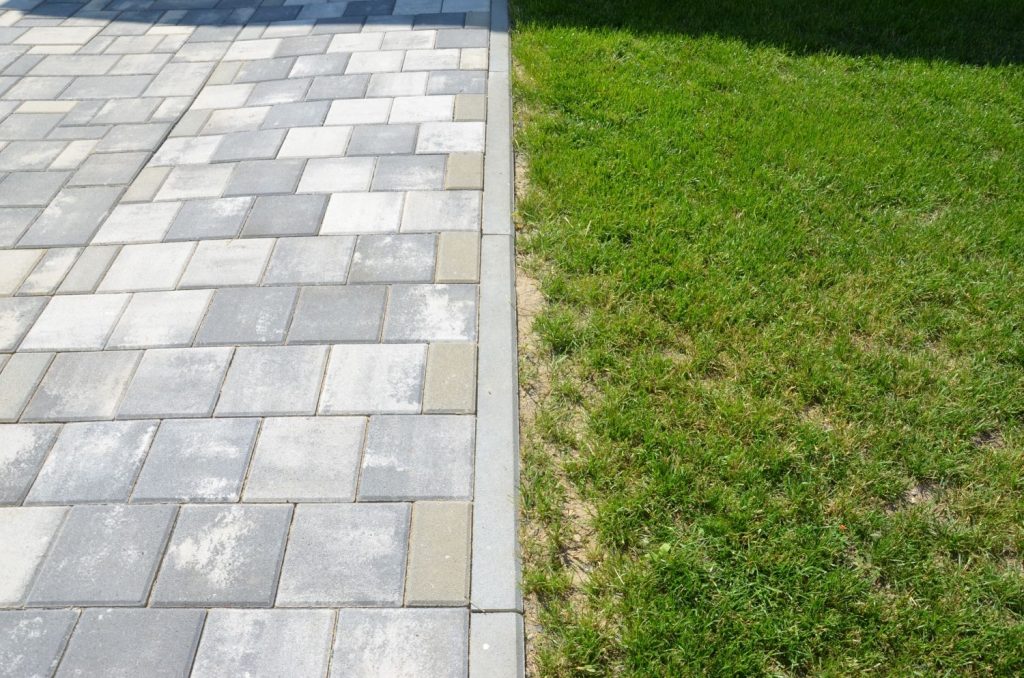Betonová zámková dlažba s chodníkovým obrubníkem vedle trávníku.